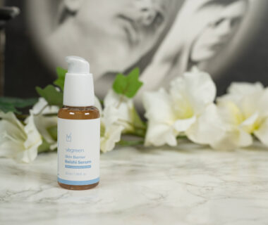 A bottle of Vegreen Skin Barrier Reishi Serum standing in front of white flowers on a dark background