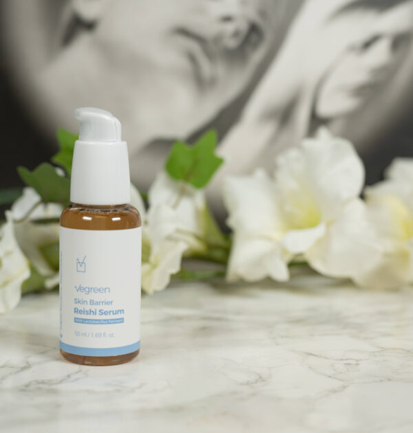 A bottle of Vegreen Skin Barrier Reishi Serum standing in front of white flowers on a dark background