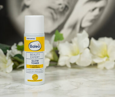 A bottle of Balea Beauty Expert Glow Toner standing in front of a dark background with white flowers