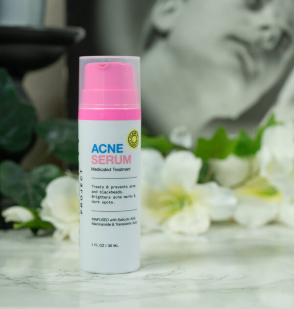 A bottle of innbeauty Project Acne Treatment Review standing in front of a drak background with white flowers